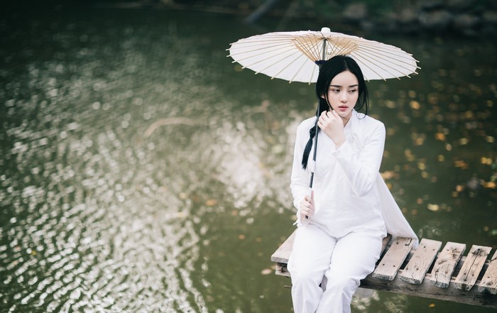 Woman in white dress holding umbrella on wooden pier