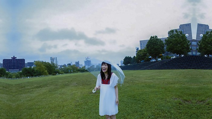 Woman with umbrella on a grassy hill with buildings in background