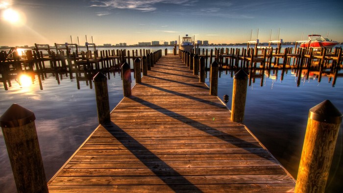Wooden pier at sunset with boats and city skyline