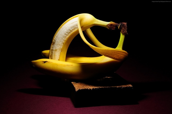 Two bananas, one peeled, on a dark background