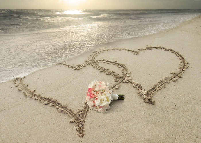 Two hearts drawn in sand with wedding bouquet on beach