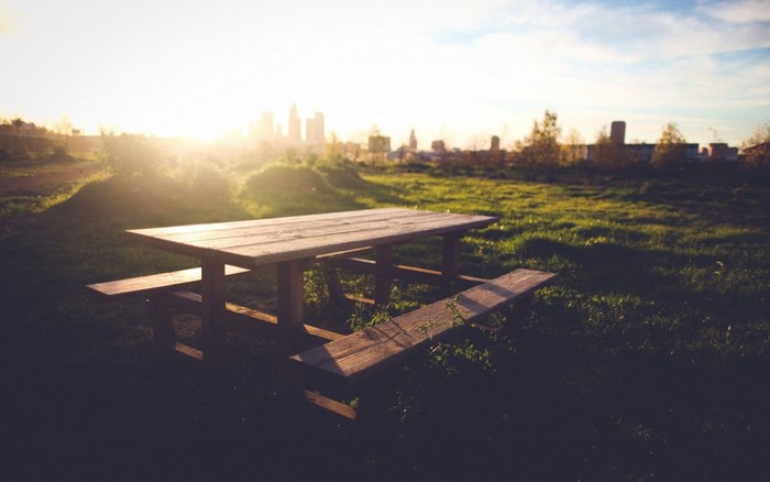 Picnic table in a field at sunset with city skyline