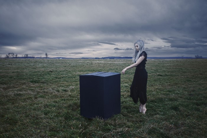 Woman in black dress with black cube in field