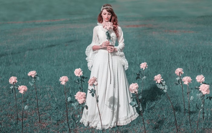 Woman in white dress holding a rose in a field of flowers
