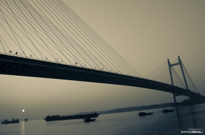 Cable-stayed bridge over a river at sunset with boats