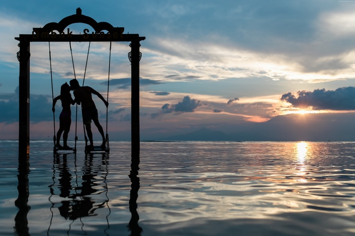 Couple kissing on a swing at sunset over the sea
