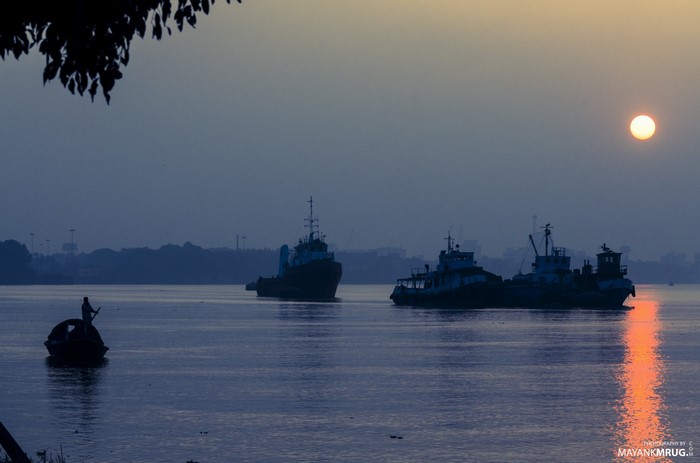 Boats on a river at sunset with a lone rower