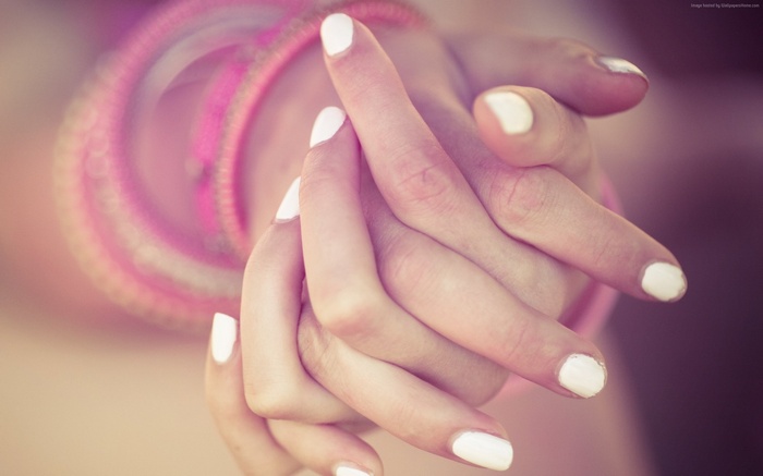 Hands with white nail polish and pink bracelets
