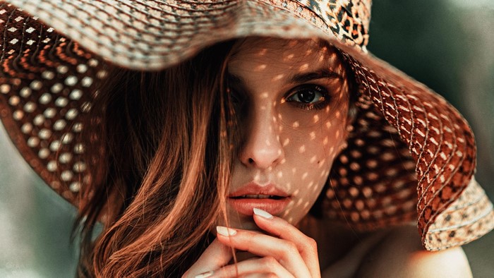 Woman wearing a wide-brimmed hat with dappled light on her face