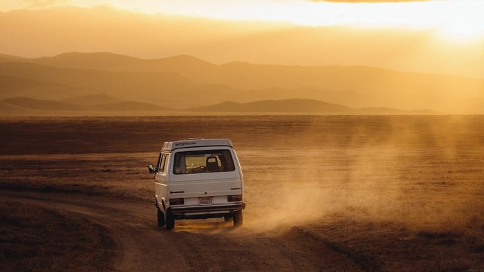 White van driving on a dirt road at sunset