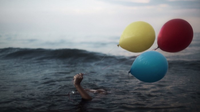 Person drowning in sea holding balloons