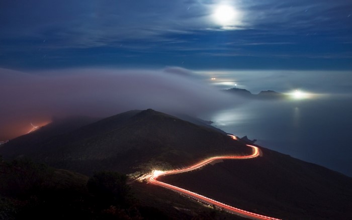 Nighttime mountain road with fog and moonlight