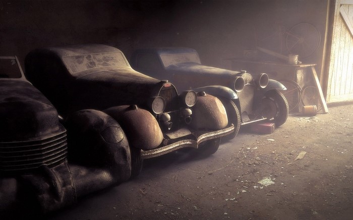 Vintage cars covered in dust in a dimly lit garage