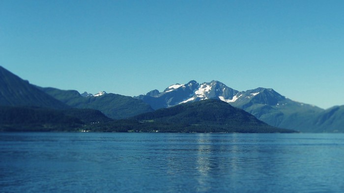 Snow-capped mountains rise above a calm blue sea.
