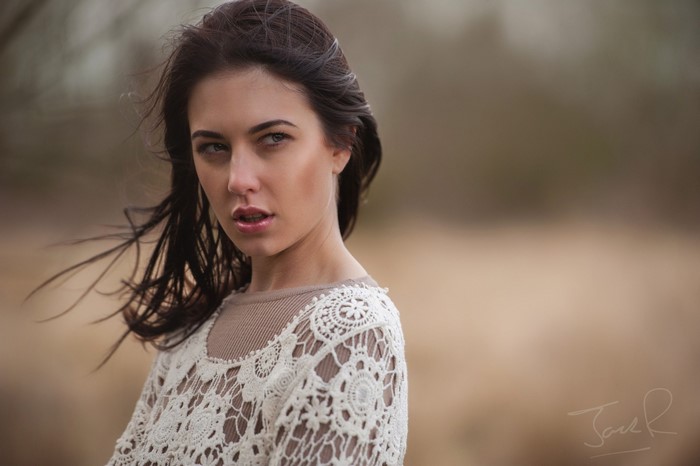 Woman with long brown hair wearing a white lace top