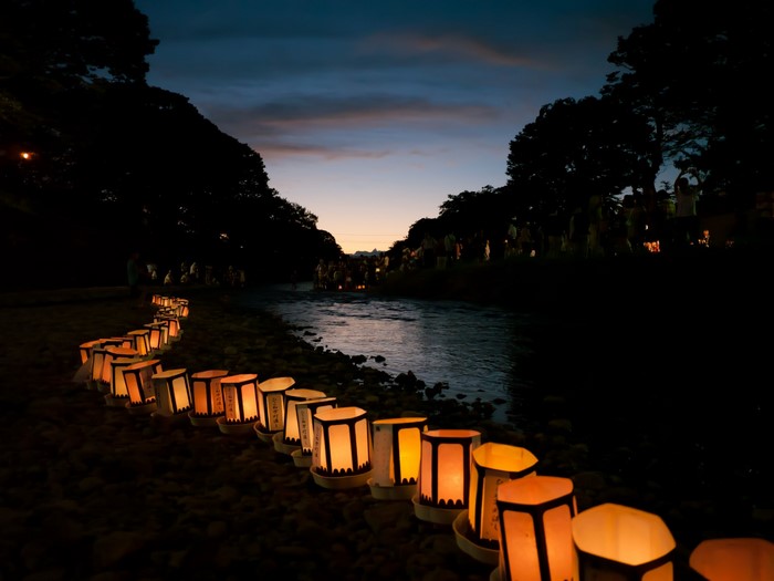 Paper lanterns line a riverbank at dusk in Japan