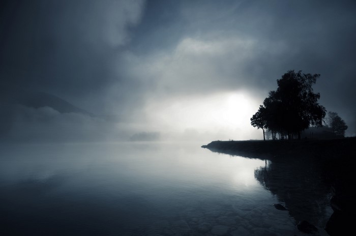 Misty lake with trees and mountains at dawn