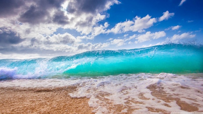 Turquoise wave crashing on a sandy beach under a cloudy sky