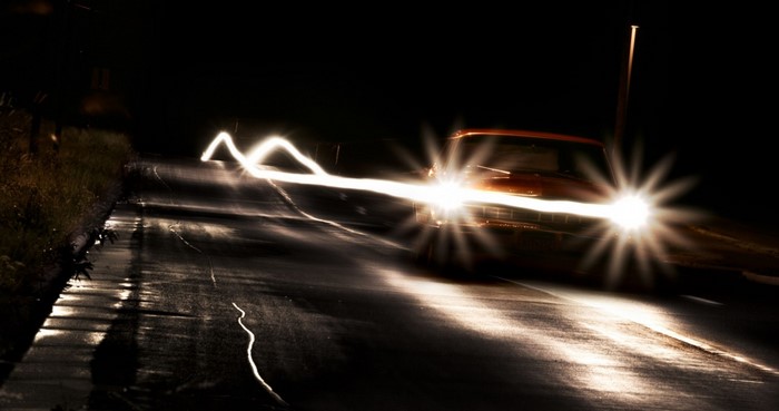 Car headlights on a dark, wet road at night