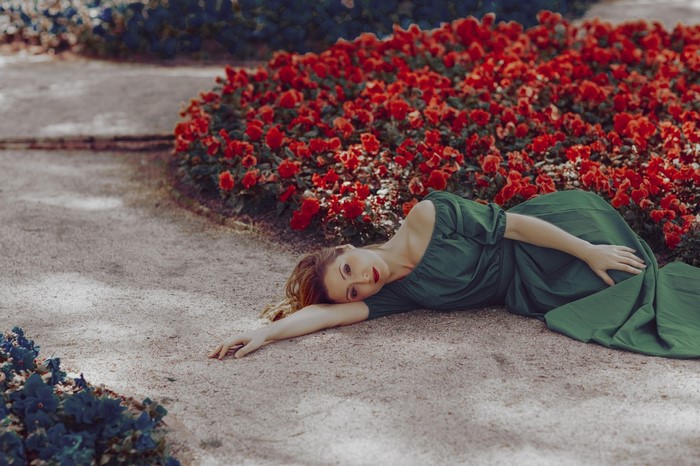 Woman in green dress lying in a garden with red flowers