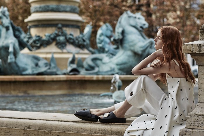 Woman in white outfit sitting by a fountain with statues