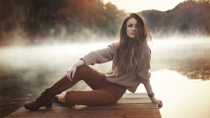 Woman sitting on a wooden dock by a misty lake