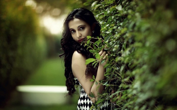Woman peeking through green leaves in a garden