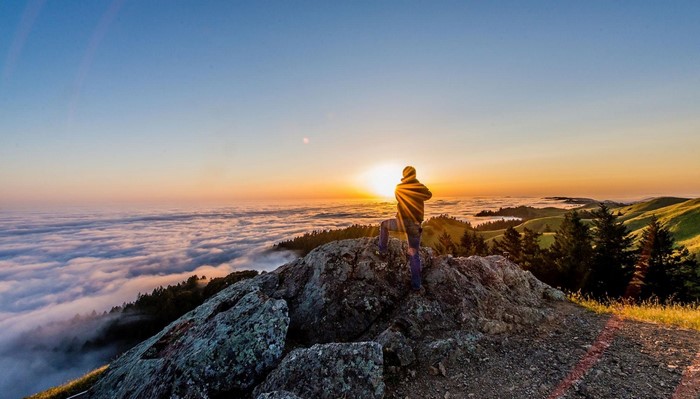 Man on mountain peak overlooking clouds at sunrise