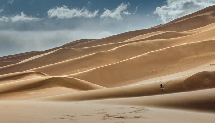 Person walking on sand dunes under a cloudy sky