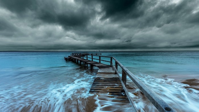 Wooden pier extending into the ocean under stormy clouds