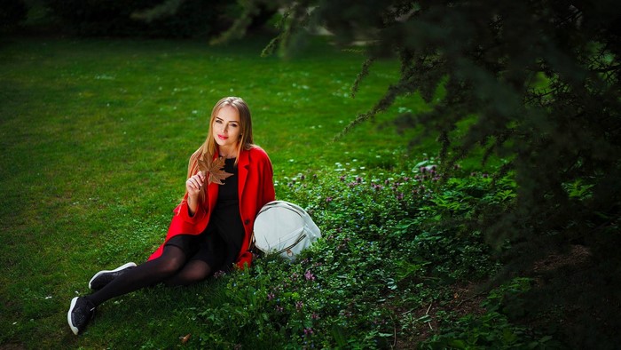 Woman in red coat holding a leaf in a park