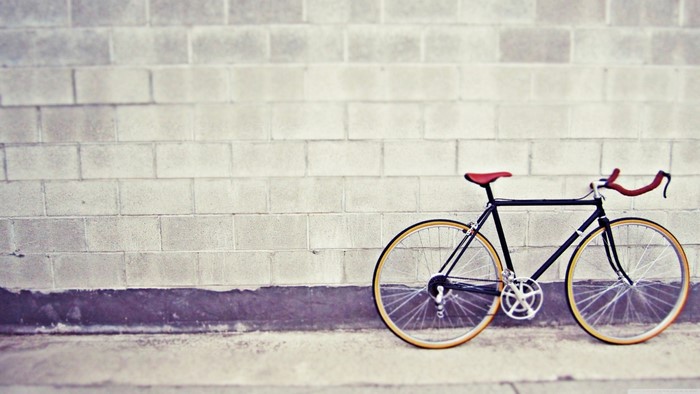 Black bicycle with red seat and handlebars against a brick wall