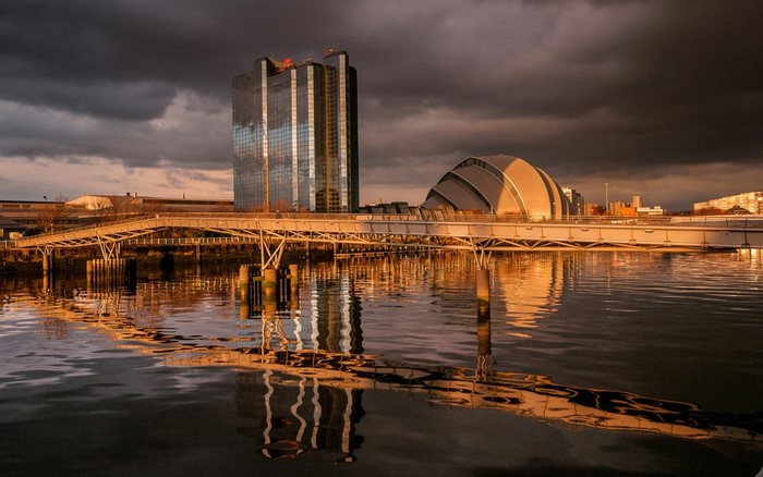 Cityscape with skyscraper, dome building, and bridge over water at sunset