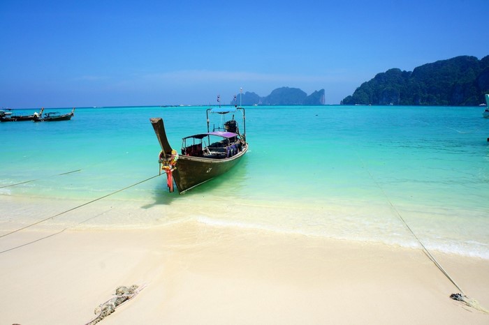 Longtail boat anchored in turquoise water off a sandy beach