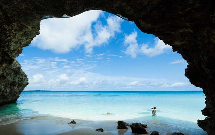 Cave view of a beach with a person and baby in the water