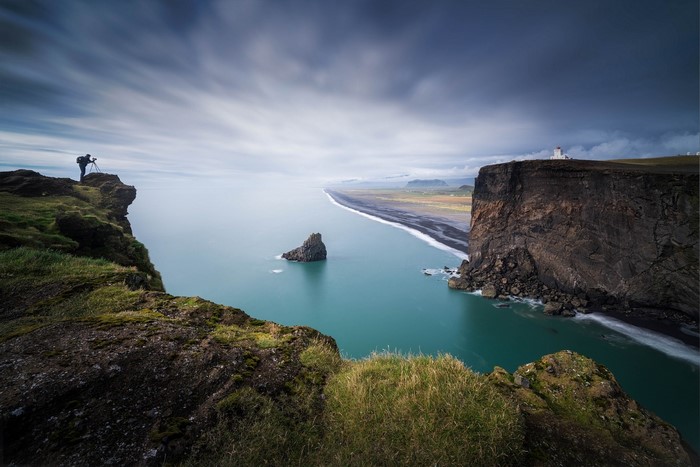 Photographer on cliff overlooking black sand beach and sea stacks in Iceland