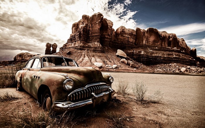 Abandoned vintage car in a desert landscape with rock formations