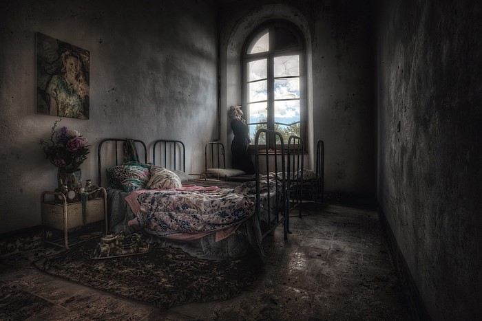 Abandoned bedroom with a woman looking out a window
