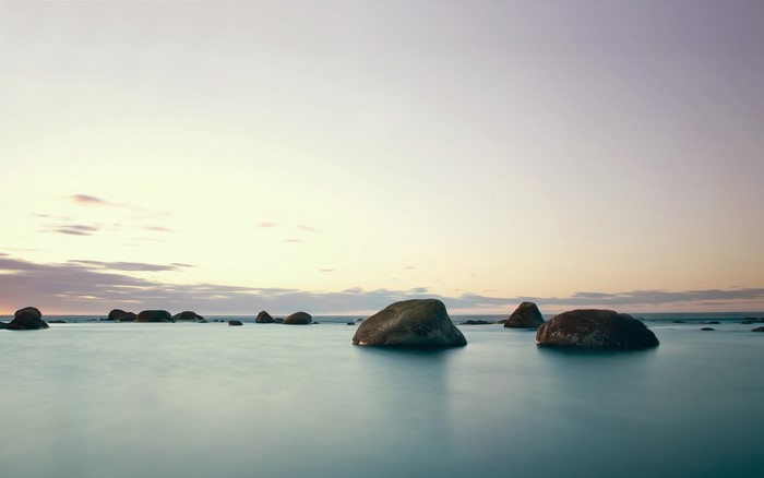Ocean rocks at sunset with calm water and clouds