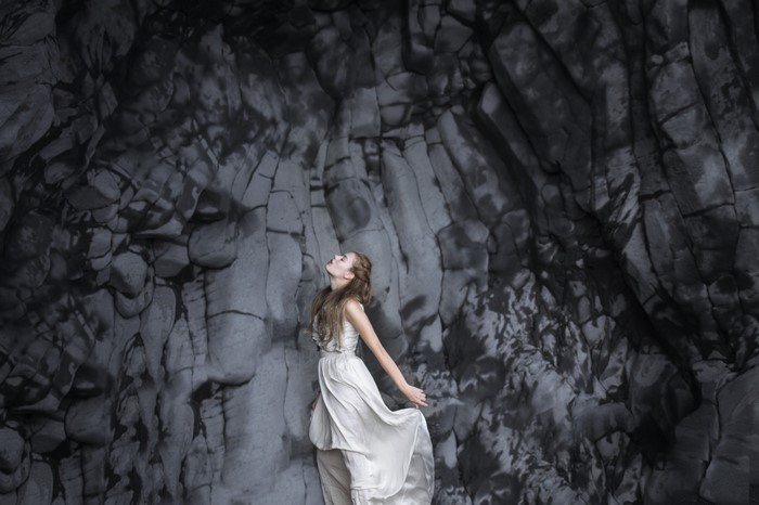Woman in white dress against dark rock formation
