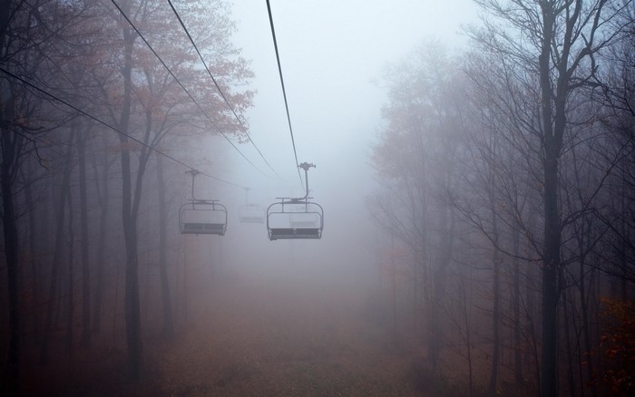 Ski lift chairs in a foggy forest during fall