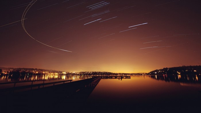 Star trails over a city and lake at night