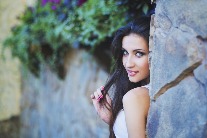 Woman with dark hair peeking from behind a stone wall