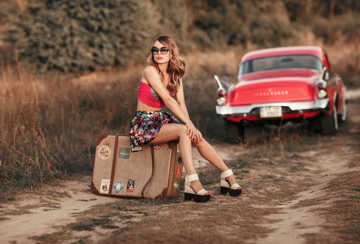 Woman sitting on suitcases near a vintage red car