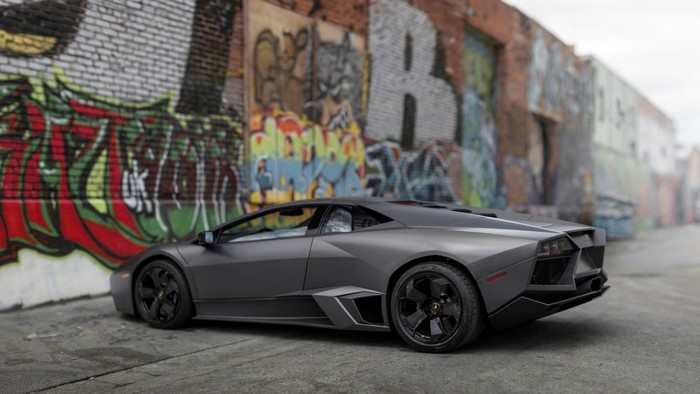 Matte gray Lamborghini Reventon parked against graffiti wall