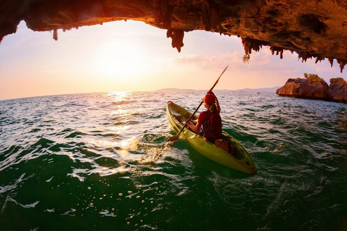 Woman kayaking in the sea at sunset near a cave