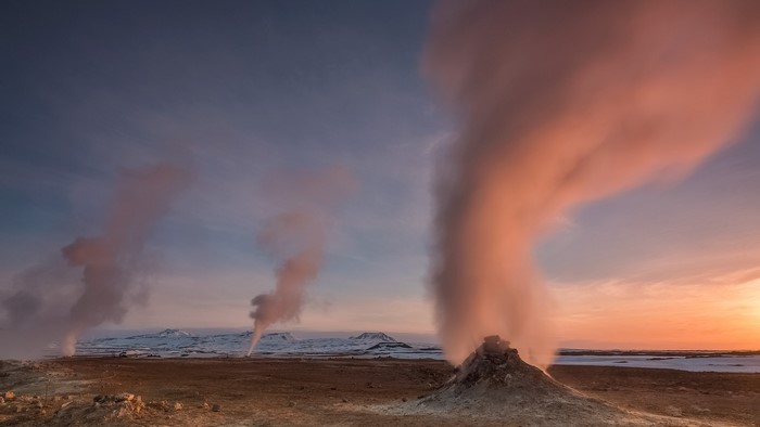 Geysers erupting steam at sunset in a volcanic landscape
