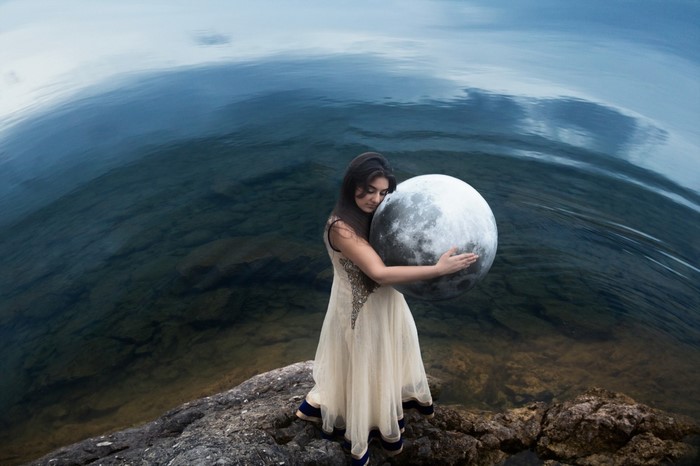 Woman holding a large moon by the sea