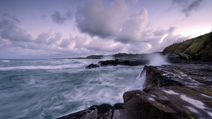 Waves crashing on rocky shore with cloudy sky