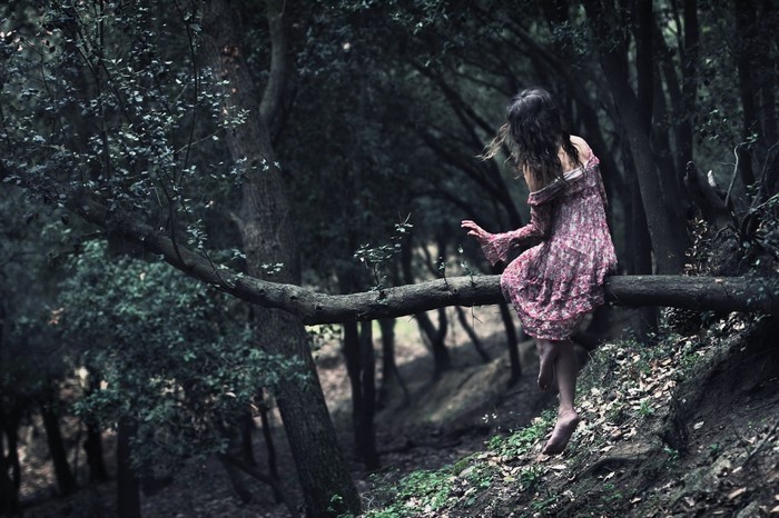 Woman in a dress sitting on a tree branch in a dark forest